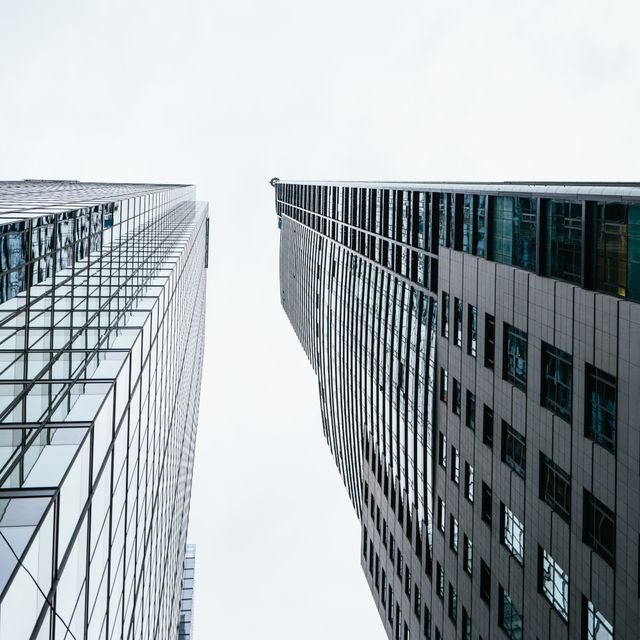 Viewed from below, modern skyscrapers stretch towards the cloudy sky, emphasizing urban architecture and city life. Suitable for illustrating corporate environments, city landscapes, and architectural design concepts. Ideal for business presentations, real estate promotions, and urban planning materials.