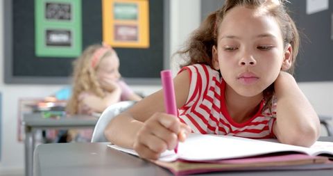 Focused biracial girl writing at classroom desk