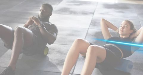 Training partners rolling out core with foam rollers and block in bright gym studio