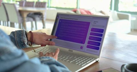 Male pointing at laptop and typing in denim jacket at home using chat ai interface with smartphone