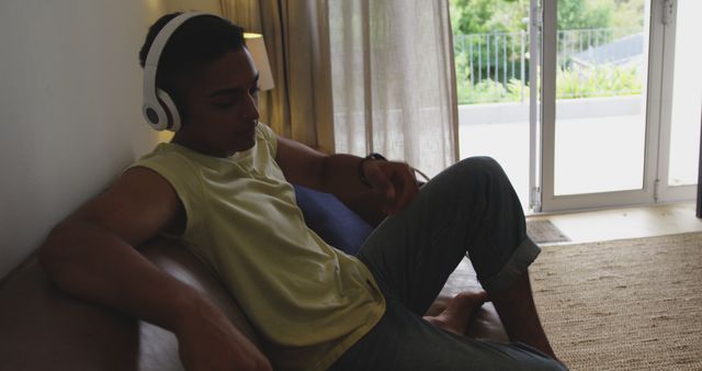 Man sitting on sofa indoors, wearing headphones, immersed in listening. Suitable for use in lifestyle blogs, articles about relaxation, advertisements for home audio equipment, and images related to leisure and downtime.