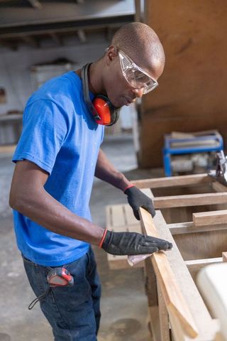 Carpenter sanding wood plank on workbench in industrial workshop showing precision