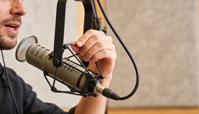 Podcast host adjusting broadcast microphone shock mount with xlr cable close-up