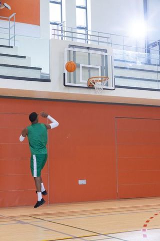 Player jumping and shooting basketball toward hoop in indoor gym with orange wall