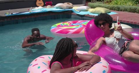 African american friends lounging on colorful pool floats enjoying backyard summer party