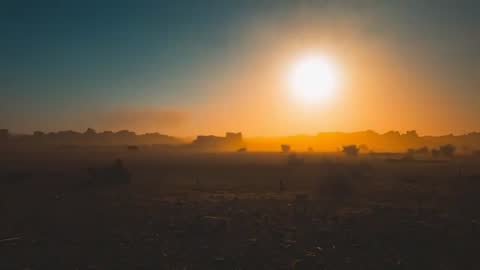 Sun Rising Over Hazy Desert Plain at Dawn Revealing Silhouetted Rock Formations and Debris