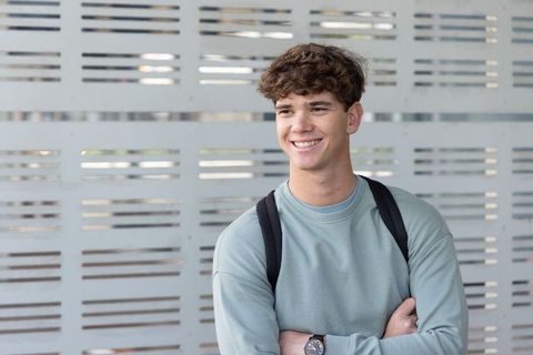 Smiling college student wearing backpack standing against modern perforated metal facade