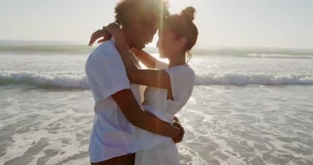 Young couple embracing and standing close to each other by the ocean at sunrise. The warm, golden sunlight provides a romantic and serene atmosphere. Perfect for themes such as romance, travel, relaxation, and leisure advertising. Use in magazines, websites, or promotional materials focusing on beach vacations.