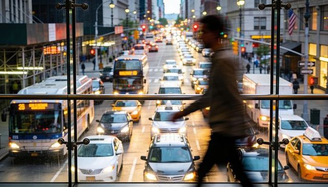 Blurred pedestrian walking through glass walkway over busy rainy city street at dusk rush-hour