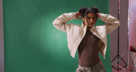 Asian model adjusting hair in beige jacket on green backdrop with rimlight fashion pose