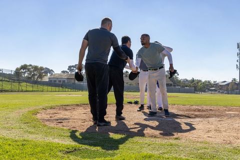 Shaking hands on pitcher's mound before game, teammates showing sportsmanship on sunny field