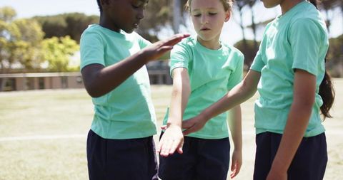 Diverse girls forming team huddle linking hands on school field showcasing teamwork