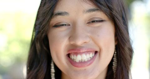 Joyful asian woman smiling closeup showing teeth with dangling earrings outdoors