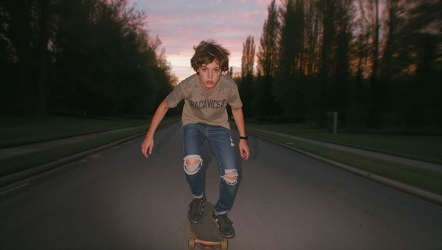 Teenage boy skateboarding at dusk through tree-lined street