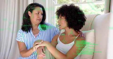 Mature woman comforting adult on sofa with neon data overlay, home caregiving moment
