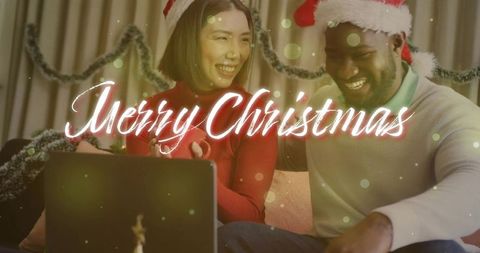 Couple celebrating virtual christmas on sofa wearing santa hats and sharing gift