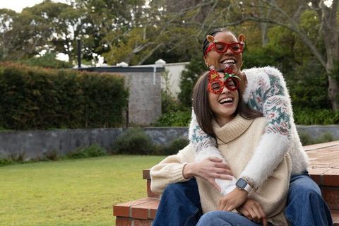 Diverse friends sharing holiday laughter wearing festive wreath and reindeer glasses
