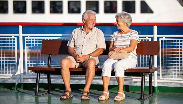 Smiling senior couple enjoying ferry deck cruise, relaxing on bench in sunshine
