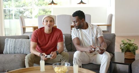 Diverse Men Playing Video Games on Couch in Bright Modern Living Room
