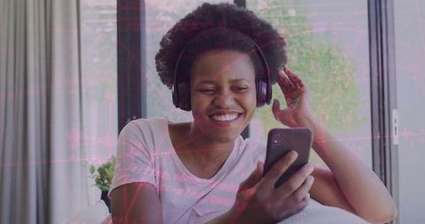Smiling woman listening to music on smartphone with wireless headphones, relaxing at home