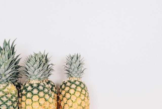 Three ripe pineapples arranged vertically against a plain white background. Ideal for use in food and beverage advertisements, tropical-themed content, healthy eating visuals, and minimalistic design projects.
