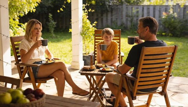Family enjoying sunny backyard breakfast on wooden patio sipping coffee with croissants