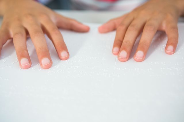 Child's hands reading braille book in classroom, highlighting tactile learning and inclusion for visually impaired students. Useful for educational materials, special needs resources, and promoting literacy for children with disabilities.