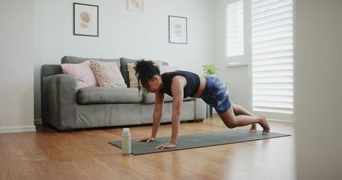 African american woman planking on yoga mat during home workout in bright living room