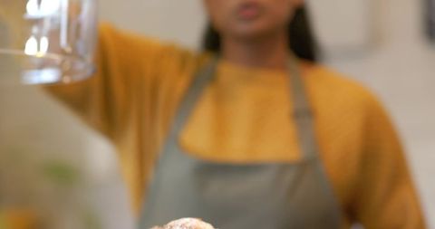 Indian female examining glass jug while presenting freshly baked pastry in cozy kitchen