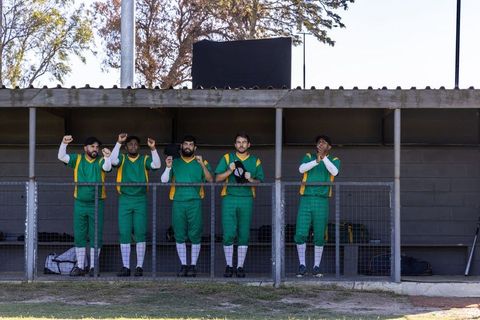 Cricket team cheering from dugout in green and yellow uniforms during sunny match