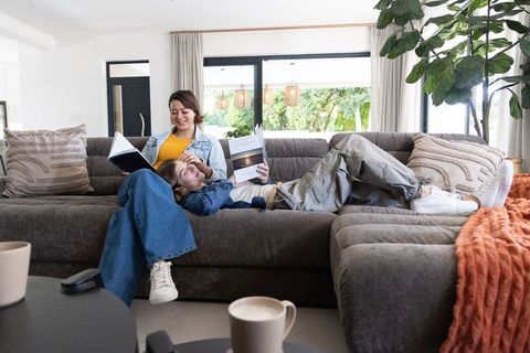 Two women lounging and reading on cozy modern grey sectional with coffee and indoor plant