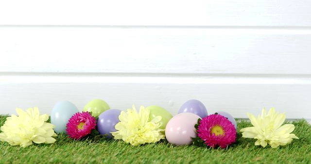 Colorful Easter eggs and bright spring flowers are arranged against a white wooden background, with copy space. This festive setup evokes the cheerful spirit of Easter celebrations and the renewal of spring.