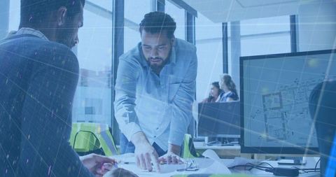 Middle eastern engineer leaning over desk pointing at blueprints in collaborative office