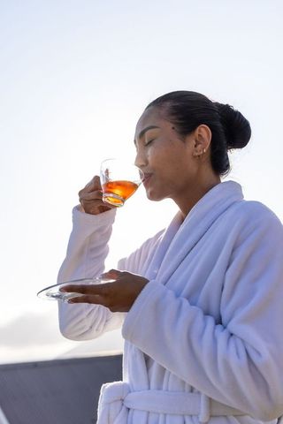 Sipping rooftop tea wearing white bathrobe backlit morning relaxation and wellness ritual