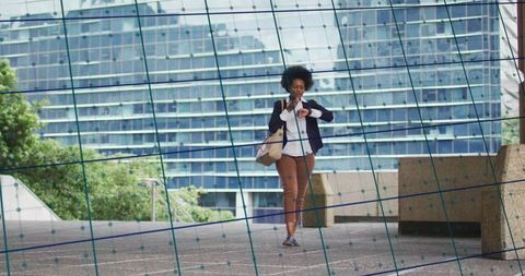 Walking professional checking watch while holding smartphone near glass office plaza