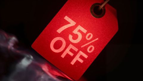 Hanging red sale tag showing 75% off, revealing textured paper and metal grommet closeup