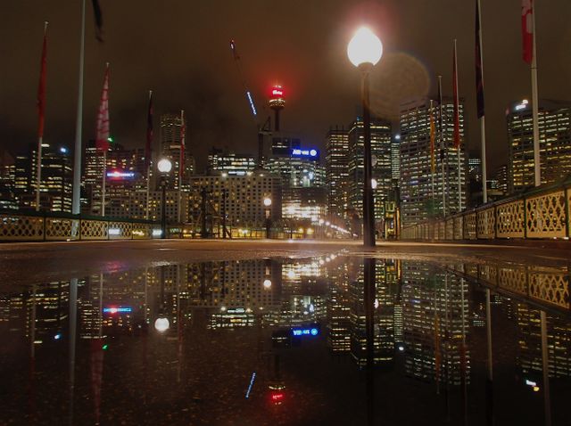 City skyline reflecting in water at night with buildings illuminated by city lights. Urban scene featuring modern architecture and vibrant city life. Suitable for themes on night cityscape, urban development, or energy of city nightlife.