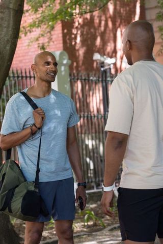 Two african american men chatting on shaded sidewalk with duffel and phone, casual urban friendship