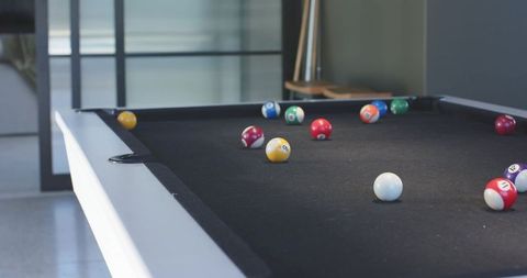 Modern pool table with black felt and scattered billiard balls in minimalist game room