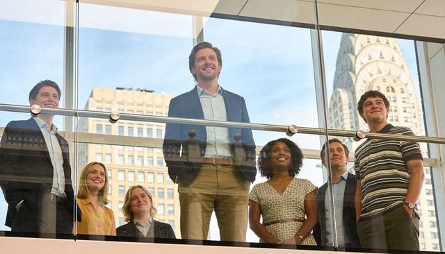Executive team standing on glass mezzanine overlooking city skyline with landmark tower