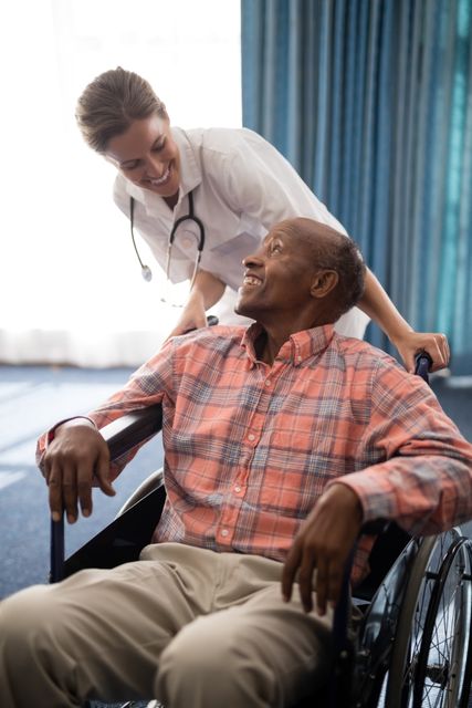 Nurse assisting elderly man in wheelchair, both smiling. Ideal for use in healthcare, senior care, retirement home, and medical care promotions. Highlights compassion, support, and professional caregiving in a medical setting.