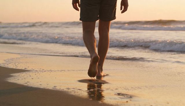 Man walking barefoot on golden beach at sunset leaving footprints in wet sand