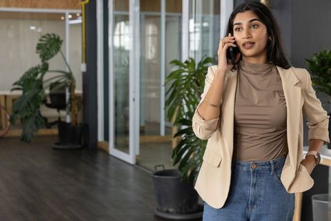 Indian businesswoman talking on smartphone in modern glass office with plants