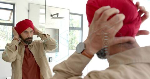 Mid-aged indian man adjusting red turban while checking mirror wearing casual wristwatch