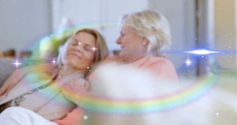 Mother and adult daughter sharing cozy sofa moment, leaning and resting with rainbow sparkle overlay