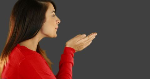 Woman in Red Sweater Blowing Kiss Against Grey Background