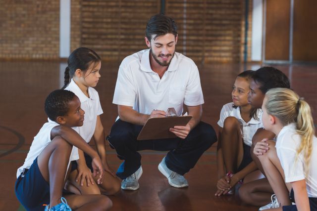 Sports teacher engaging in discussion with students in a school gym. Ideal for educational materials, school brochures, physical education programs, and articles on youth sports and coaching.