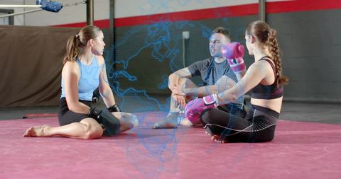 Female boxers and coach discussing training strategy on gym mat with holographic globe overlay