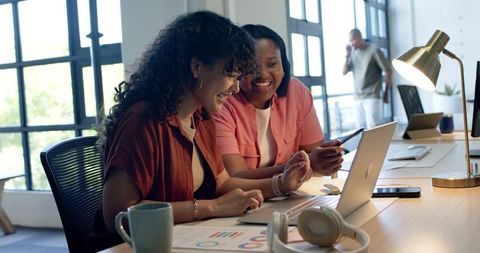African American Women Collaborating Over Analytics on Laptop in Modern Open Office