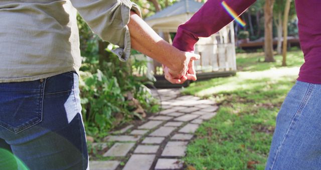 Rear view midsection of senior caucasian couple holding hands, walking in garden. happy, healthy retirement lifestyle at home.